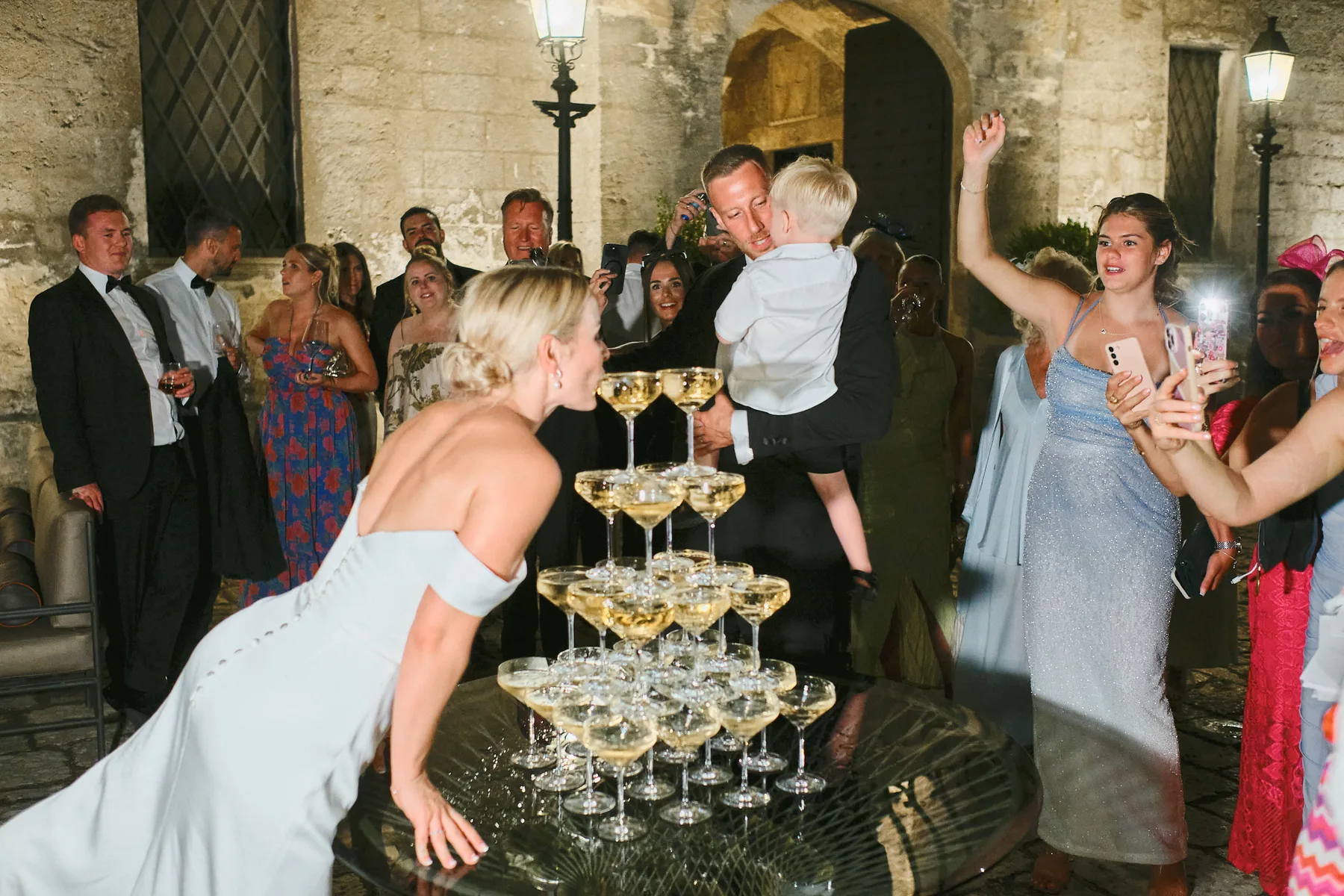 La sposa soffia sulla piramide di coppe di champagne, tra gli ospiti nel cortile di un castello