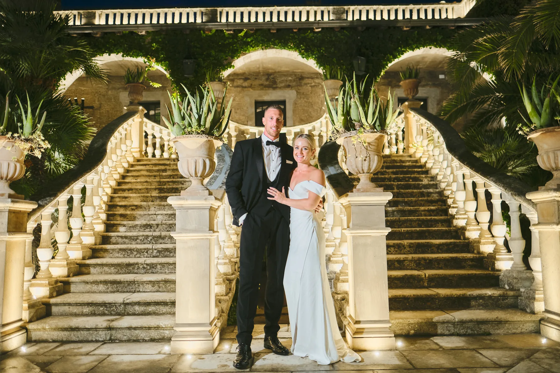 Nicholas e Grace sulla scalinata illuminata del giardino di Castello Monaci, di sera