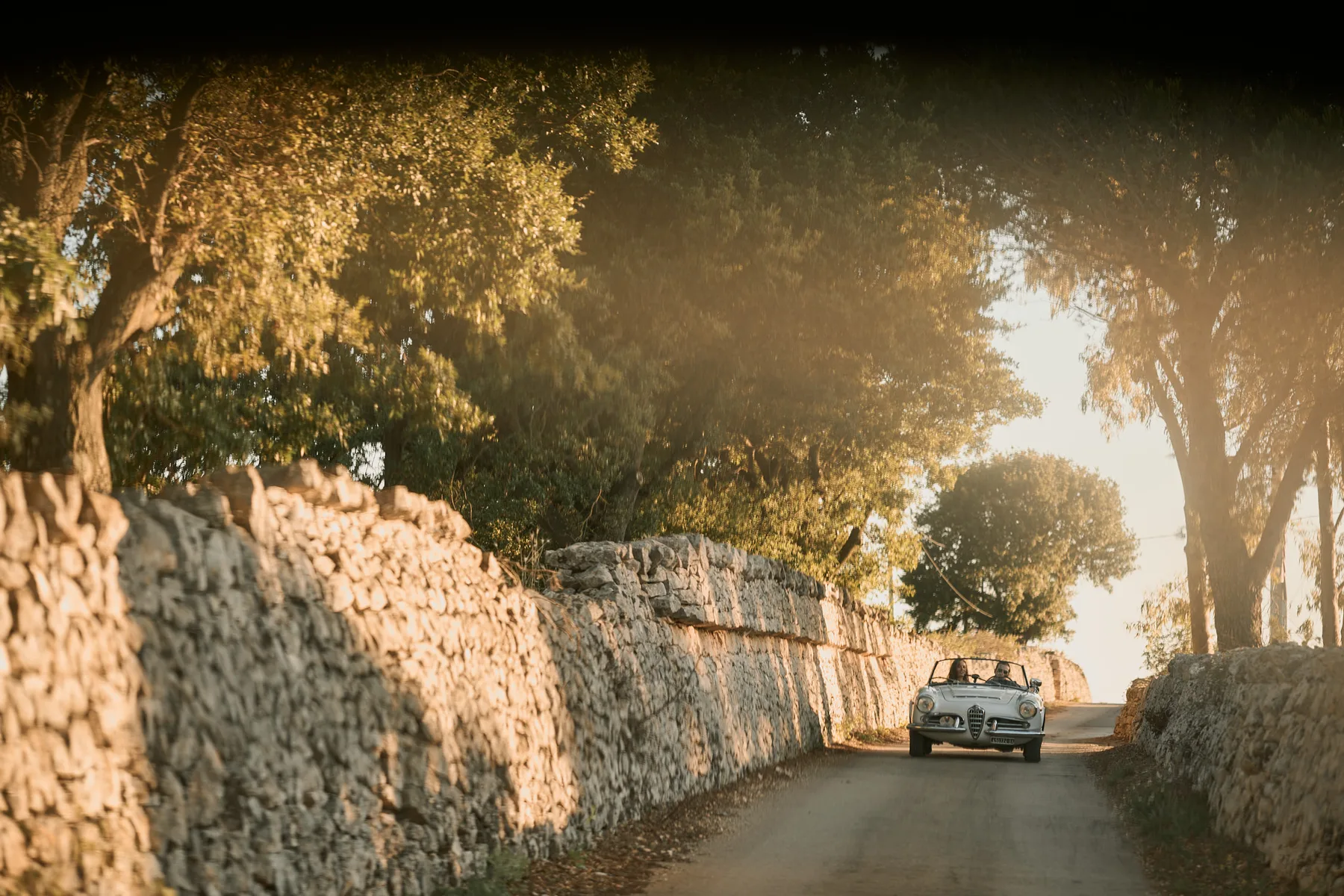 L’auto tra i muretti a secco nella luce dorata del tramonto, a Cisternino